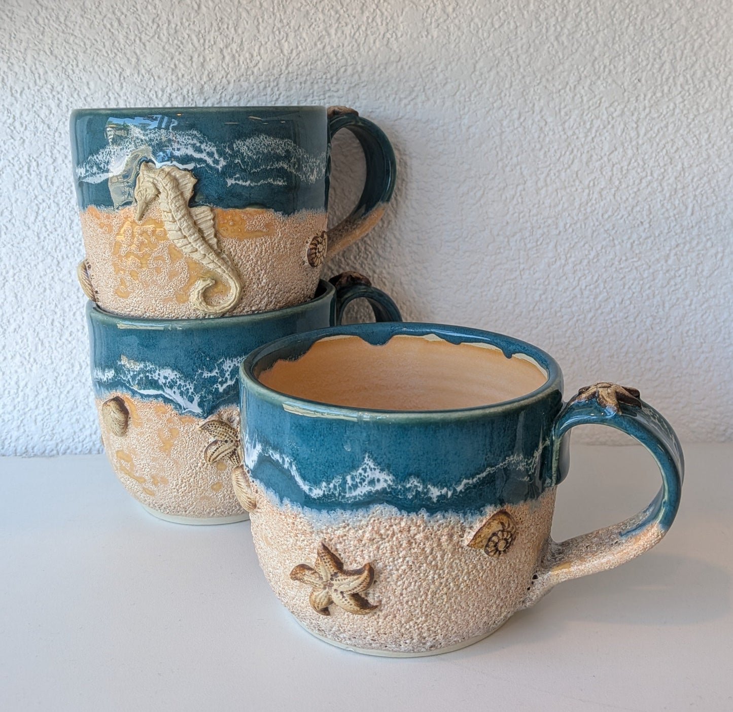 Set of ceramic mugs with ocean-themed design on a white shelf.