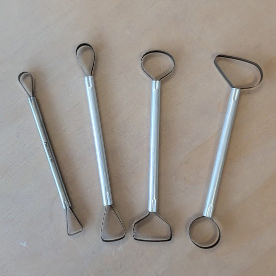 Four metal trimming tools with curved ends on a beige surface